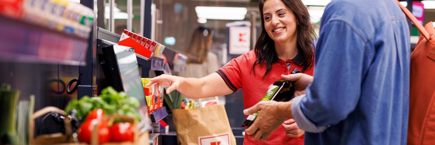 Kaufland-Verkaufsmitarbeiterin hilft einem Kunden an der SB-Kasse.