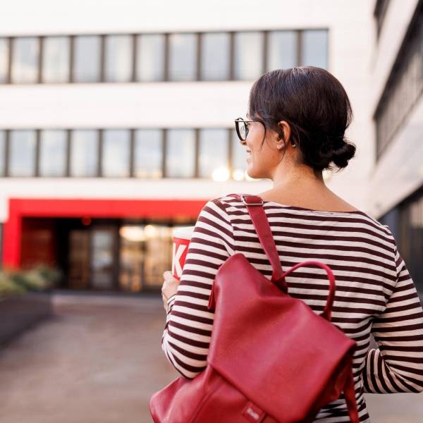Mitarbeiterin mit rotem Rucksack auf dem Weg in ein Kaufland-Bürogebäude.