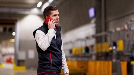 Logistik-Mitarbeiter von Kaufland telefoniert mit seinem Handy beim Gang durchs Lager.